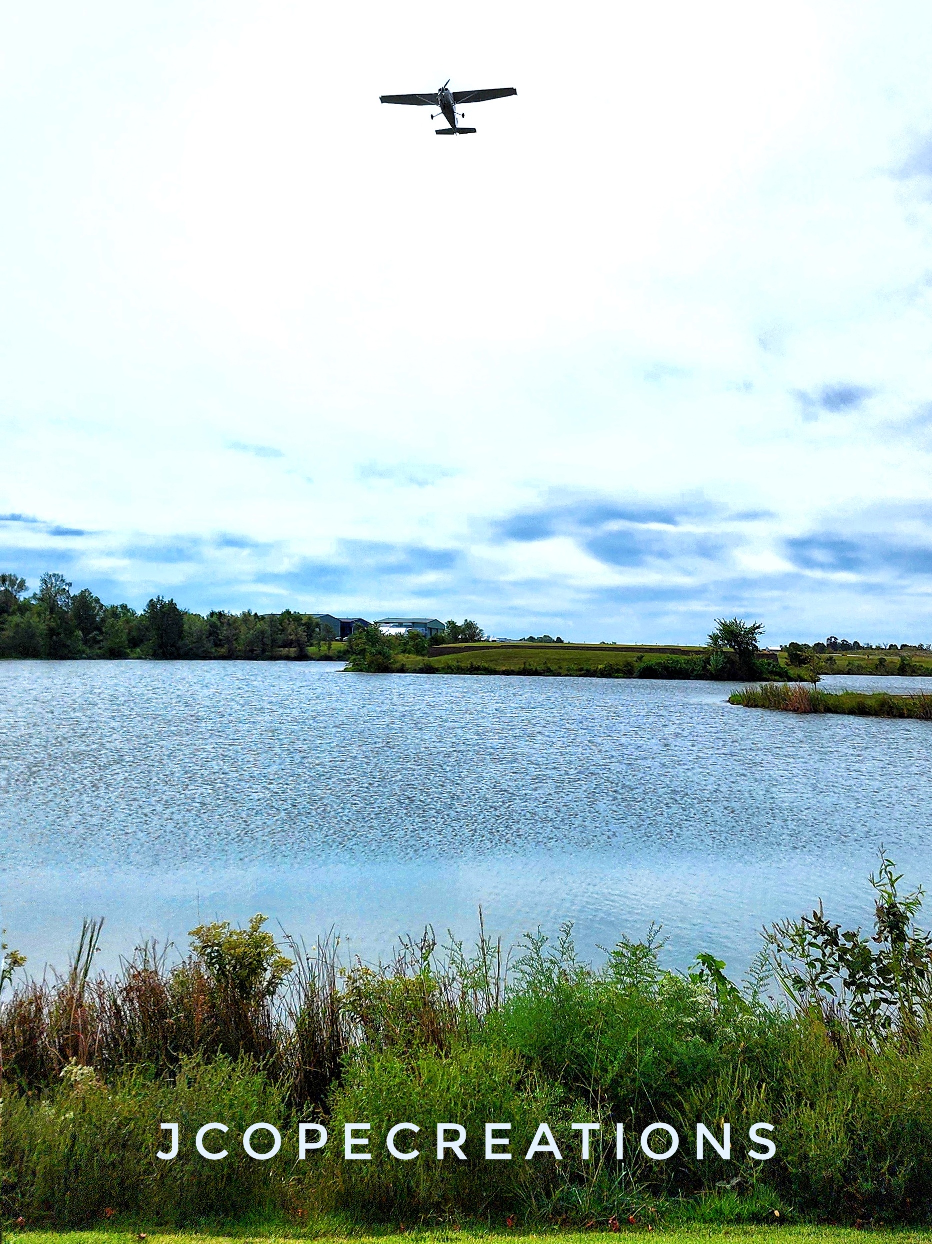A plane hovering in the clouds over a lake horizon